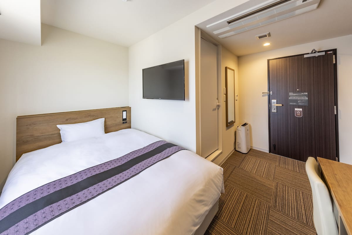 Una habitación de hotel con cama, escritorio, silla, televisión y puerta con cerradura y lector de llave.