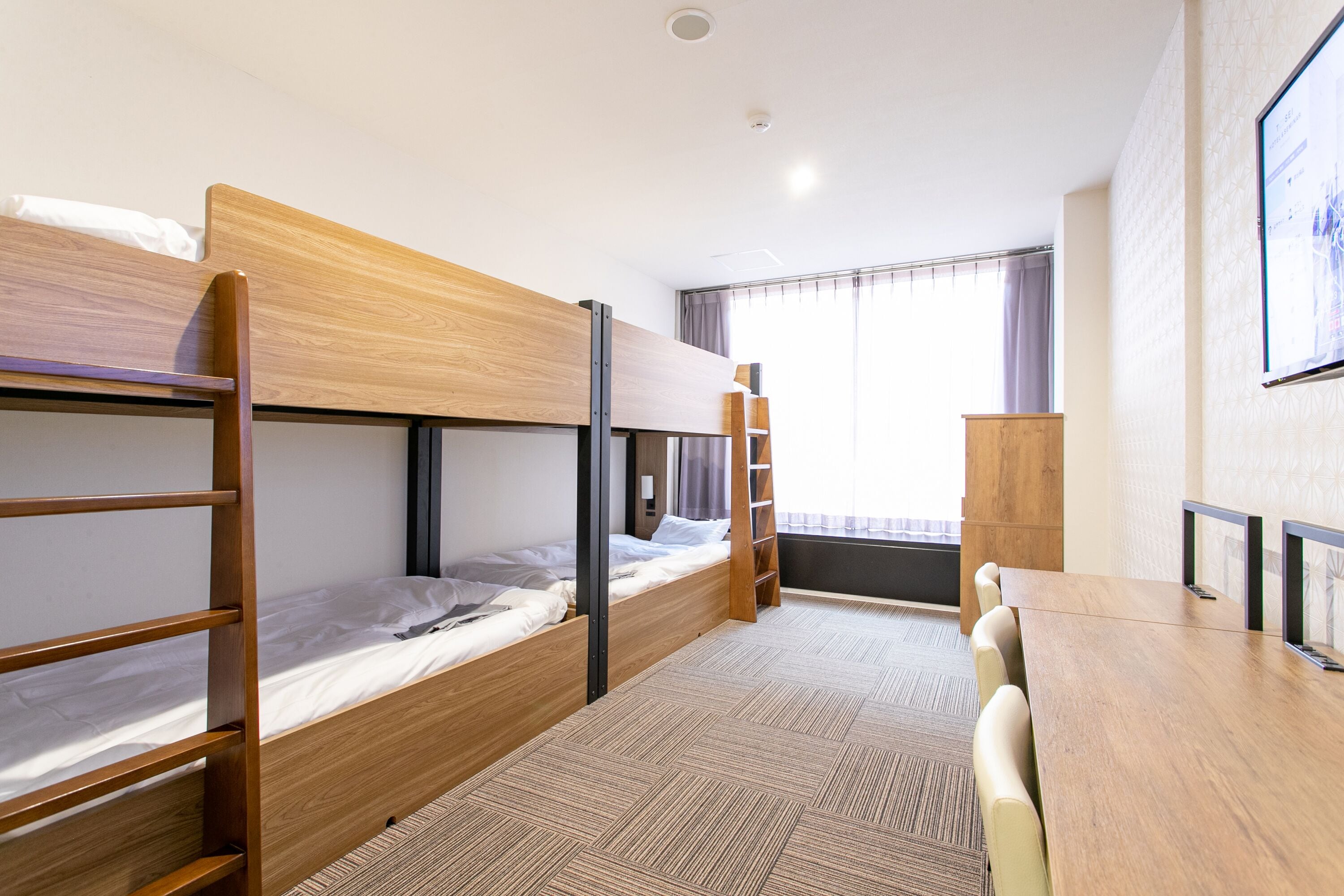 Ein Zimmer mit Etagenbetten, einem Holztisch und einem Fenster mit Vorhängen.
