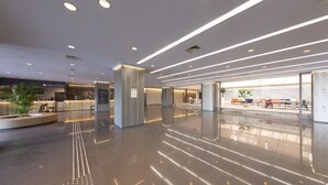 Un hall d’entrée moderne avec un sol ciré, un espace salon doté de fauteuils orange et une enseigne « Cafe COCONE ».