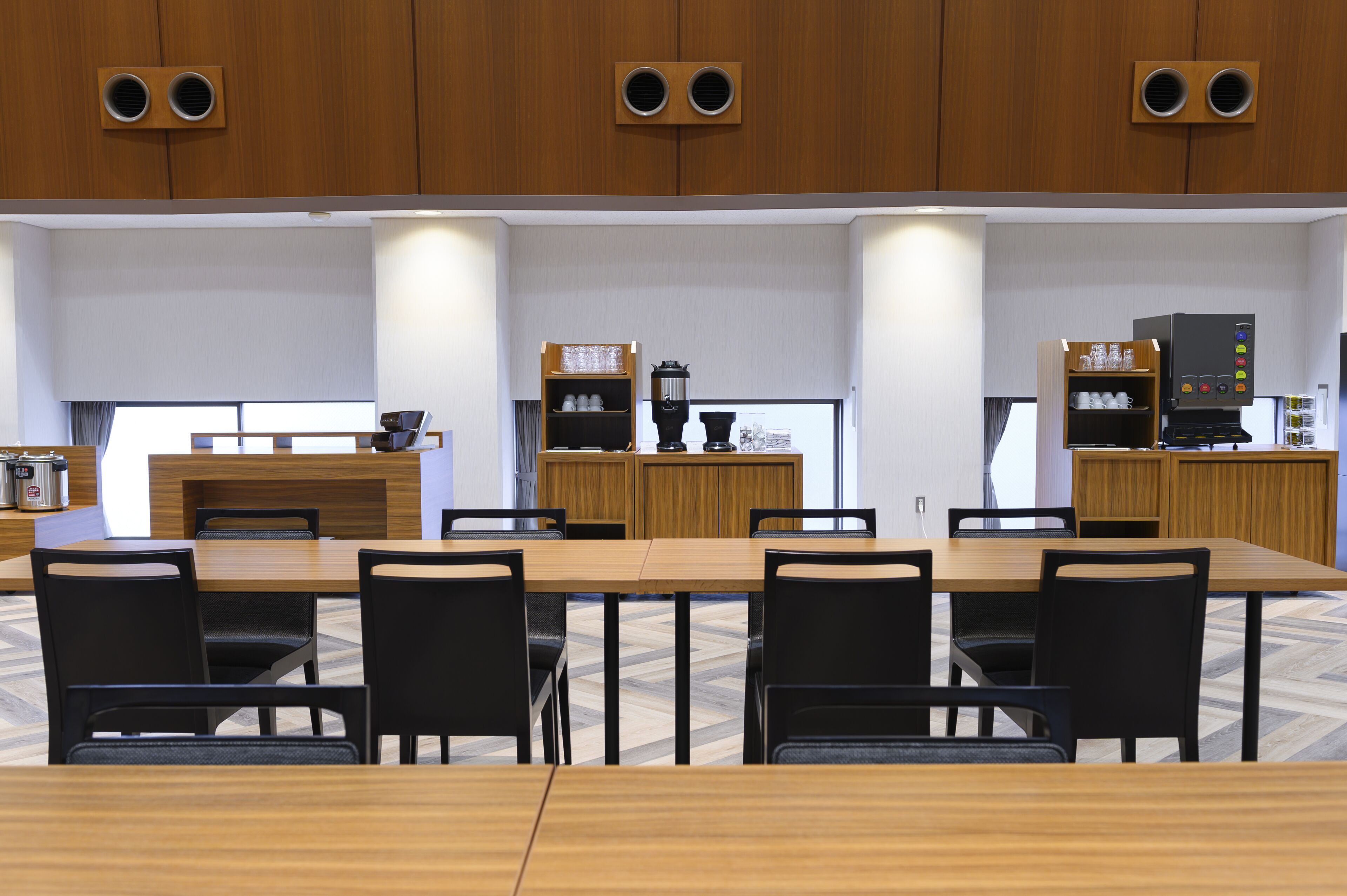 Een moderne vergaderruimte met een lange tafel, zwarte stoelen, houten kasten en een koffieapparaat.