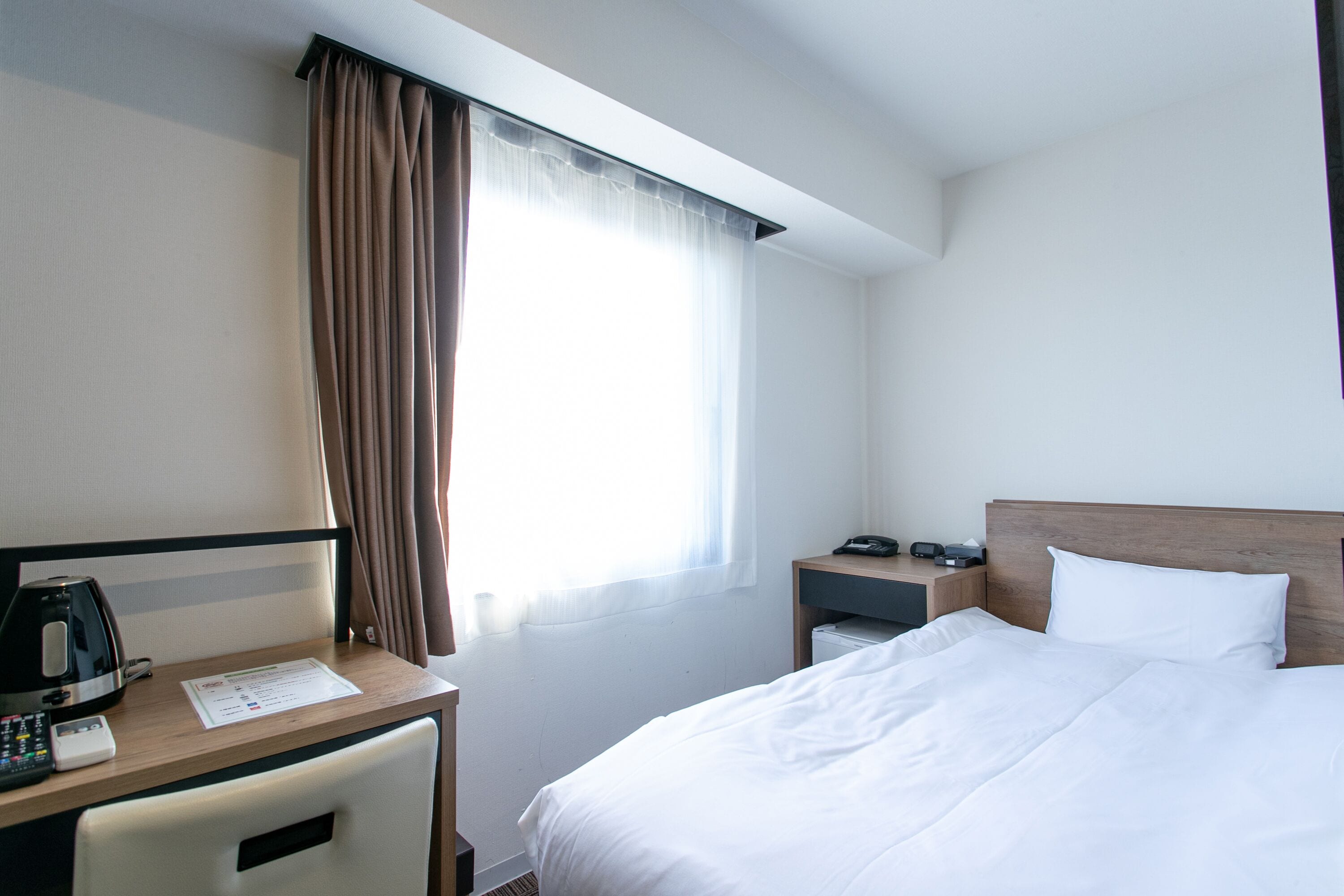 A hotel room with a bed, a desk with a coffee maker, a telephone, and a nightstand with a lamp.