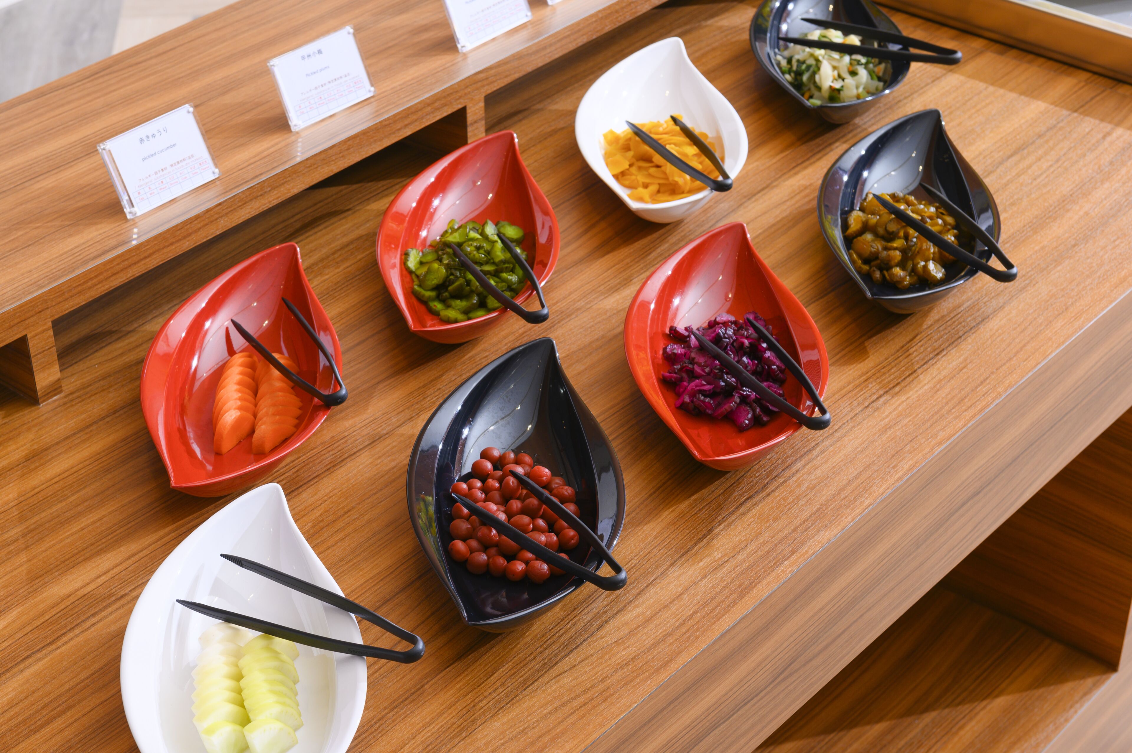 Mesa de buffet com diversos alimentos em recipientes de cores variadas.