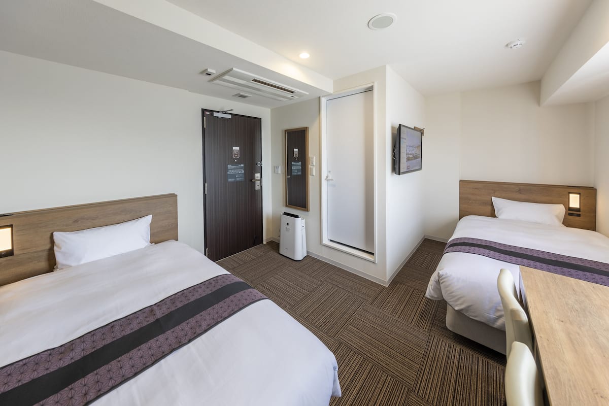 Habitación de hotel con dos camas, cabecero de madera, una mesita, un espejo y una puerta con un cartel.