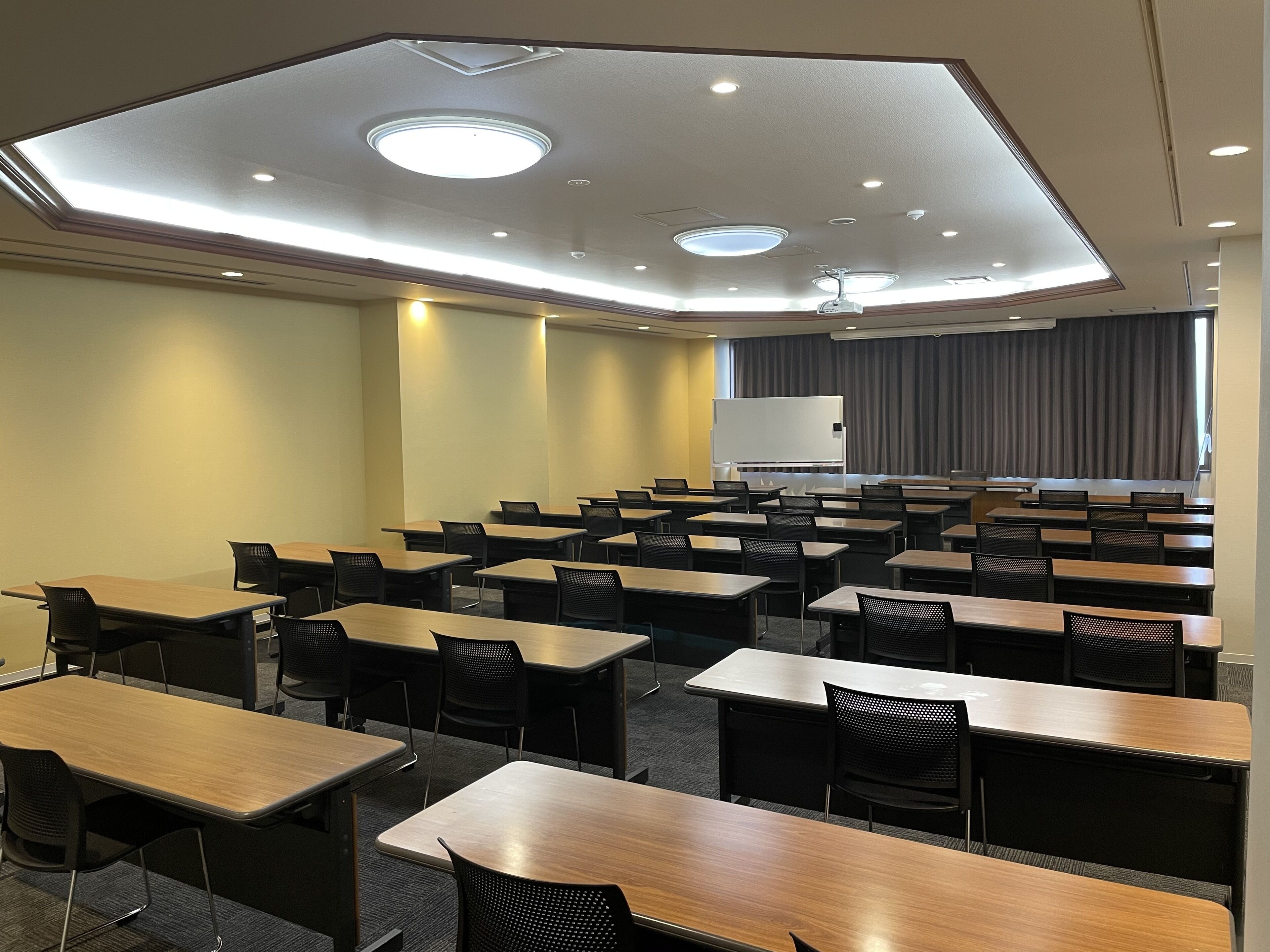 A conference room with multiple tables and chairs, a whiteboard, and a large window with curtains.