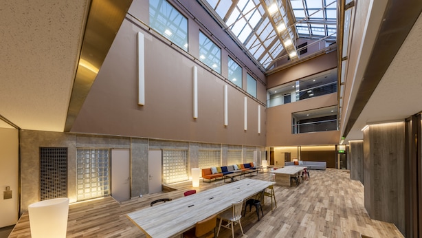 Un vaste espace intérieur doté d’un haut plafond, d’un plancher en bois et d’un coin salon central avec une longue table et des chaises.