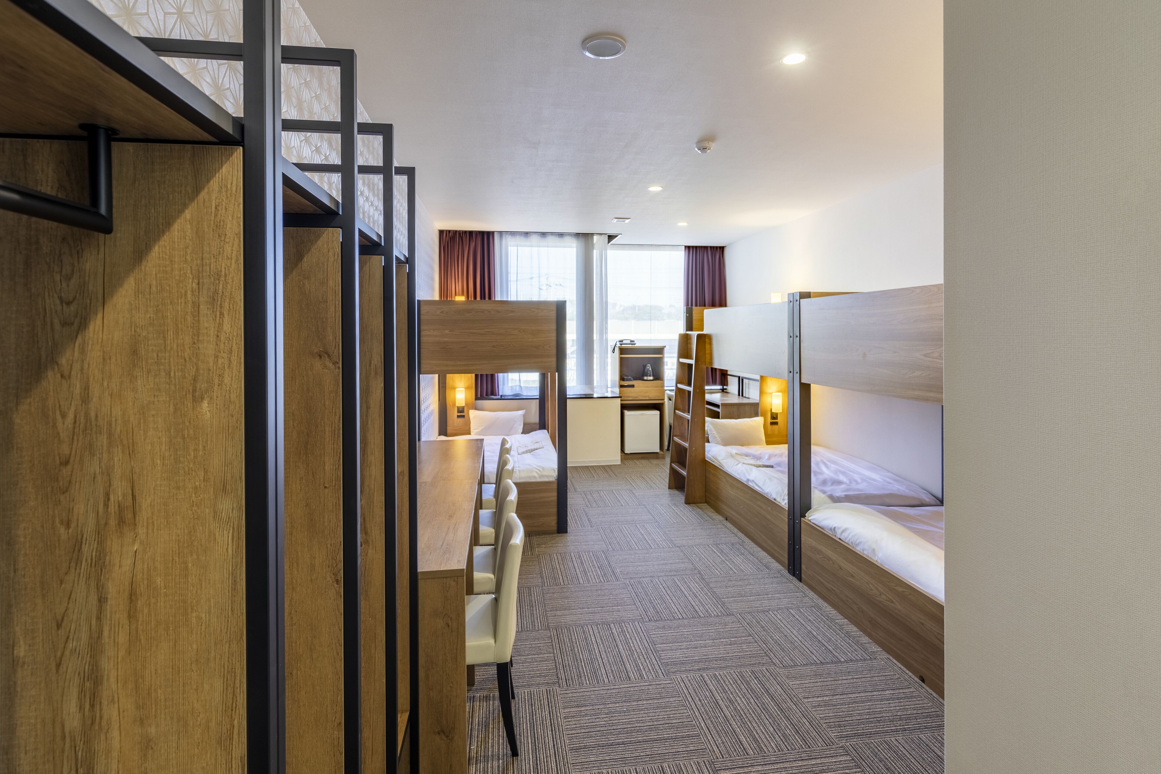 A hotel room with bunk beds, a desk, and a small kitchenette.