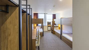 Une chambre d’hôtel avec des lits superposés, un bureau et une petite kitchenette.