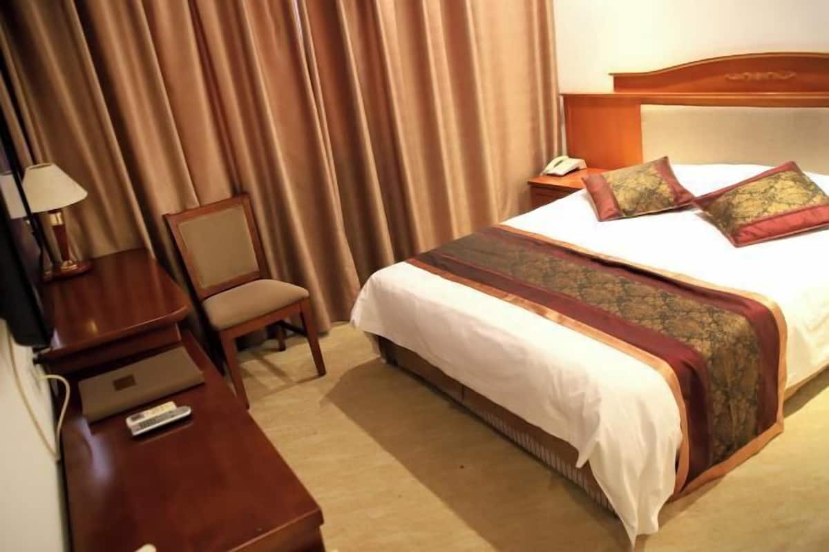 A hotel room with a bed, a chair, a desk, a lamp, and a telephone.