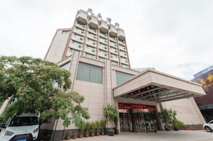 Un hotel de varios pisos con una entrada destacada, un área de estacionamiento y un edificio grande al fondo.