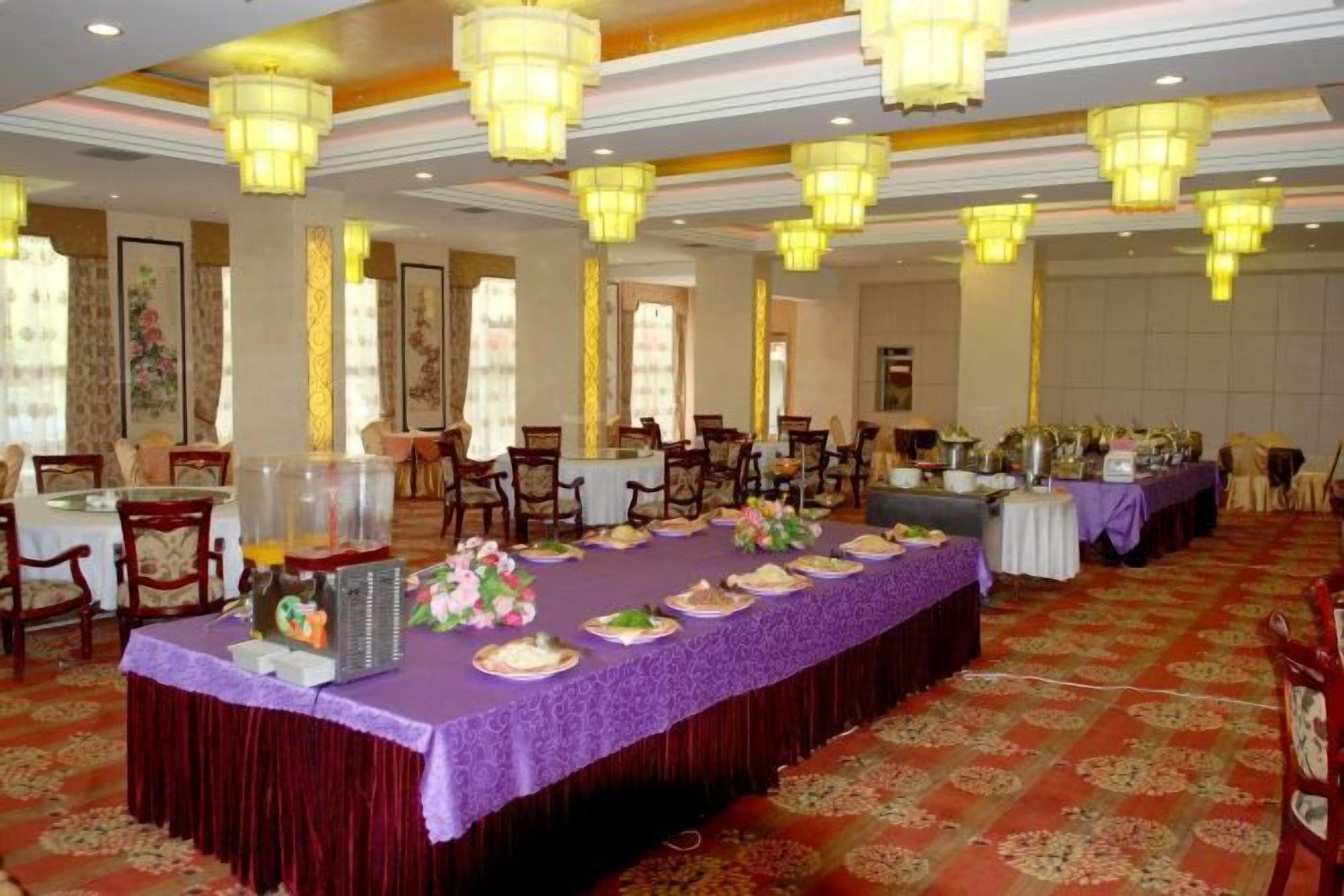 Un salón de banquetes con una larga mesa dispuesta para una comida, rodeada de sillas y un piso alfombrado.