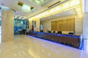 A hotel reception area with a marble counter, a large pillar, and a modern ceiling design. - Tianma Hotel (Wuwei)