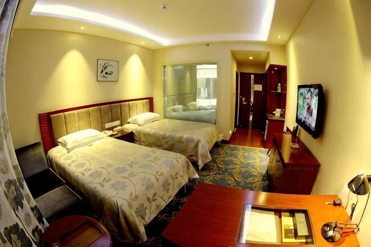 A hotel room with two beds, a desk, a chair, a TV, and a mirror.