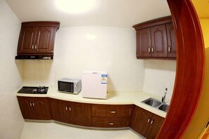 A kitchen with wooden cabinets, a microwave, and a refrigerator. - Tianma Hotel (Wuwei)