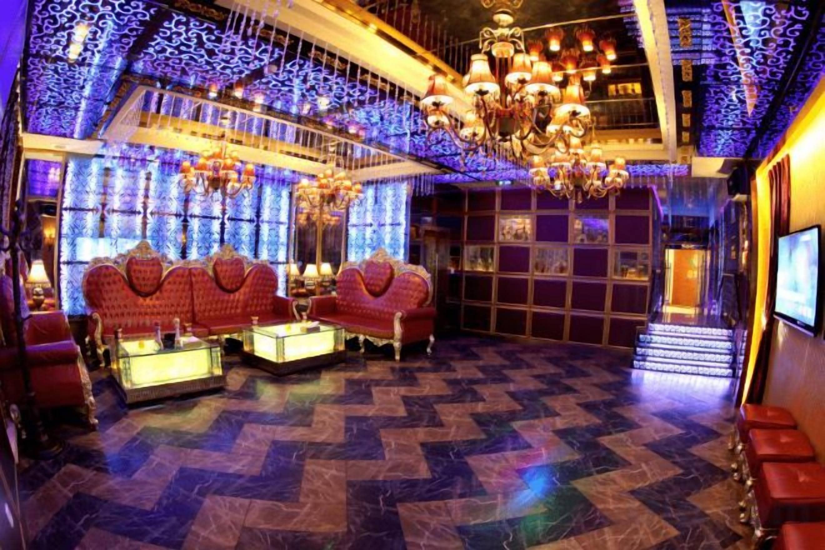 A luxurious room with a checkered floor, red sofas, a chandelier, and a large mirror.