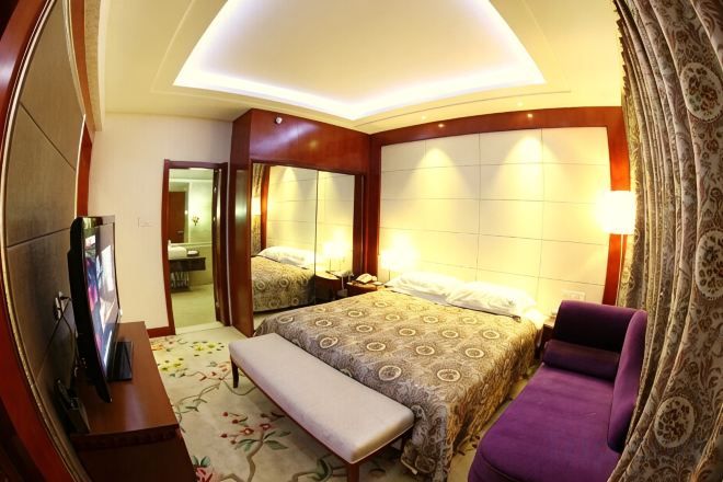 A hotel room with a bed, a bench, a TV, and a mirror.
