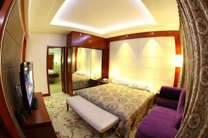 Una habitación de hotel con una cama, un banco, un televisor y un espejo.