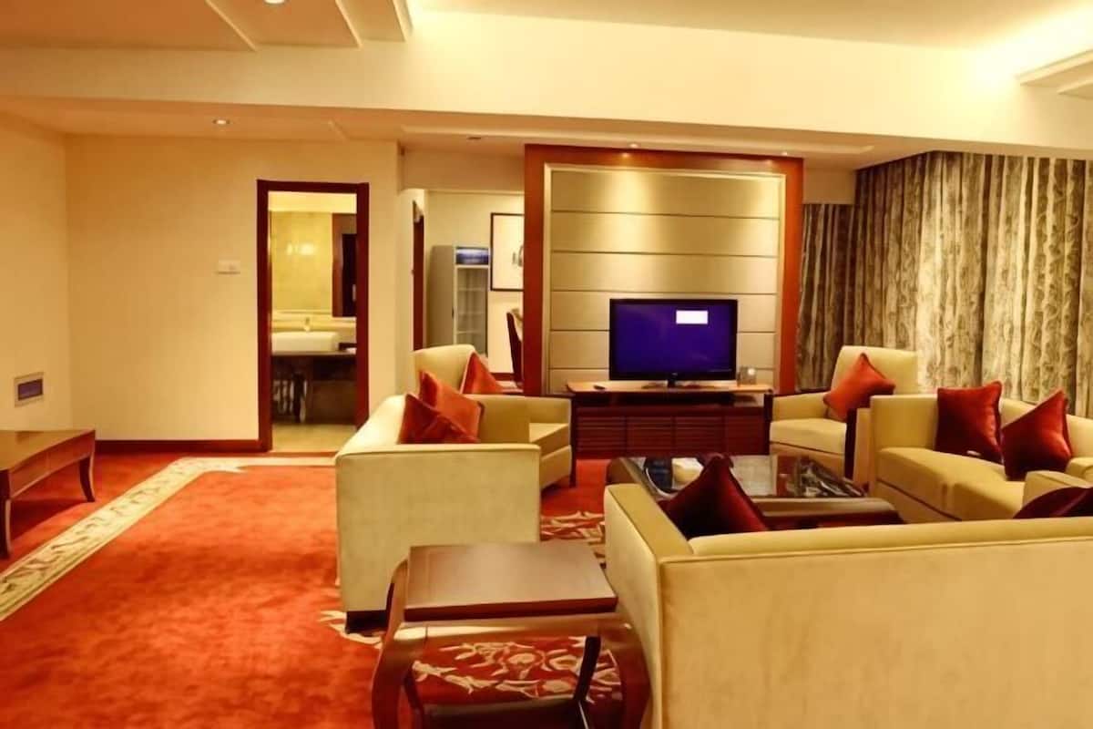 A hotel living room with a flat-screen TV, two sofas, a coffee table, and a carpeted floor.