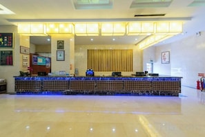 Zona de recepción de un hotel con mostrador, escritorio de recepción y extintor en la pared.