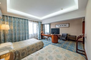 A hotel room with two beds, a desk, a chair, a television, and a wall-mounted artwork. - Tianma Hotel (Wuwei)