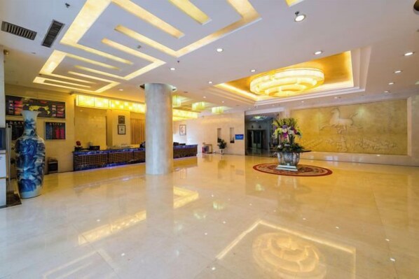 Un hall de hotel con una recepción, un jarrón grande y una pared decorativa.