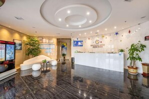 A hotel lobby with a reception desk, seating area, and a large screen.