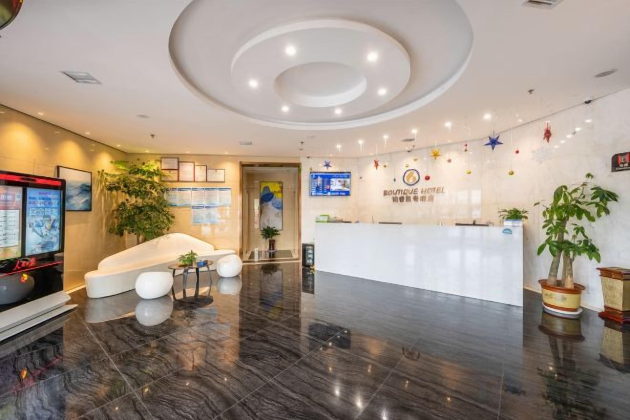 A hotel reception area with a modern design, including a reception desk, seating area, and a large plant.