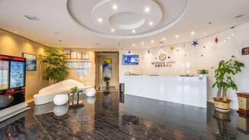 A hotel reception area with a modern design, including a reception desk, seating area, and a large plant.