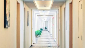 A hotel hallway with a central carpeted path, doors on both sides, and potted plants along the path.
