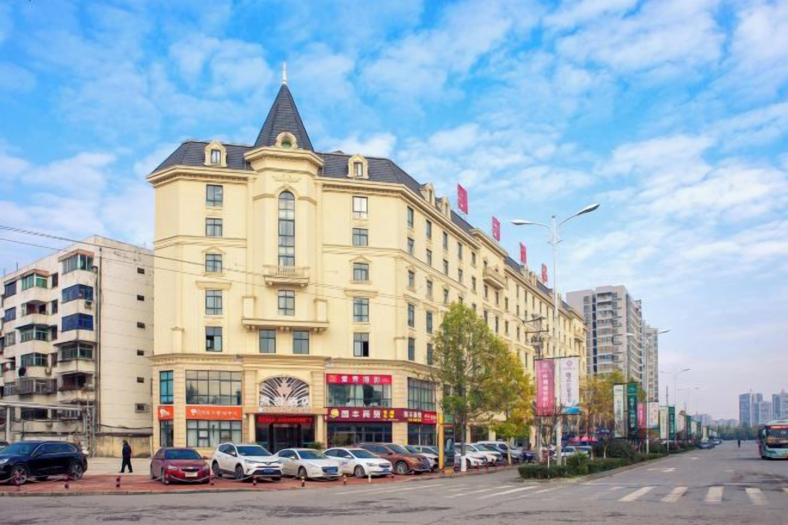 Un hotel de varios pisos con entrada en esquina, un letrero de restaurante a la vista y un estacionamiento con automóviles.
