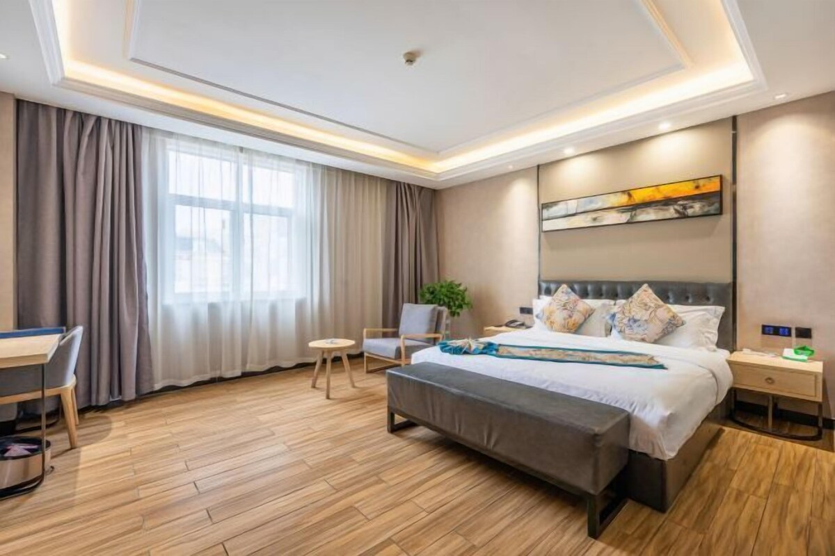 A modern hotel room with a large bed, a desk, a chair, and a small table.