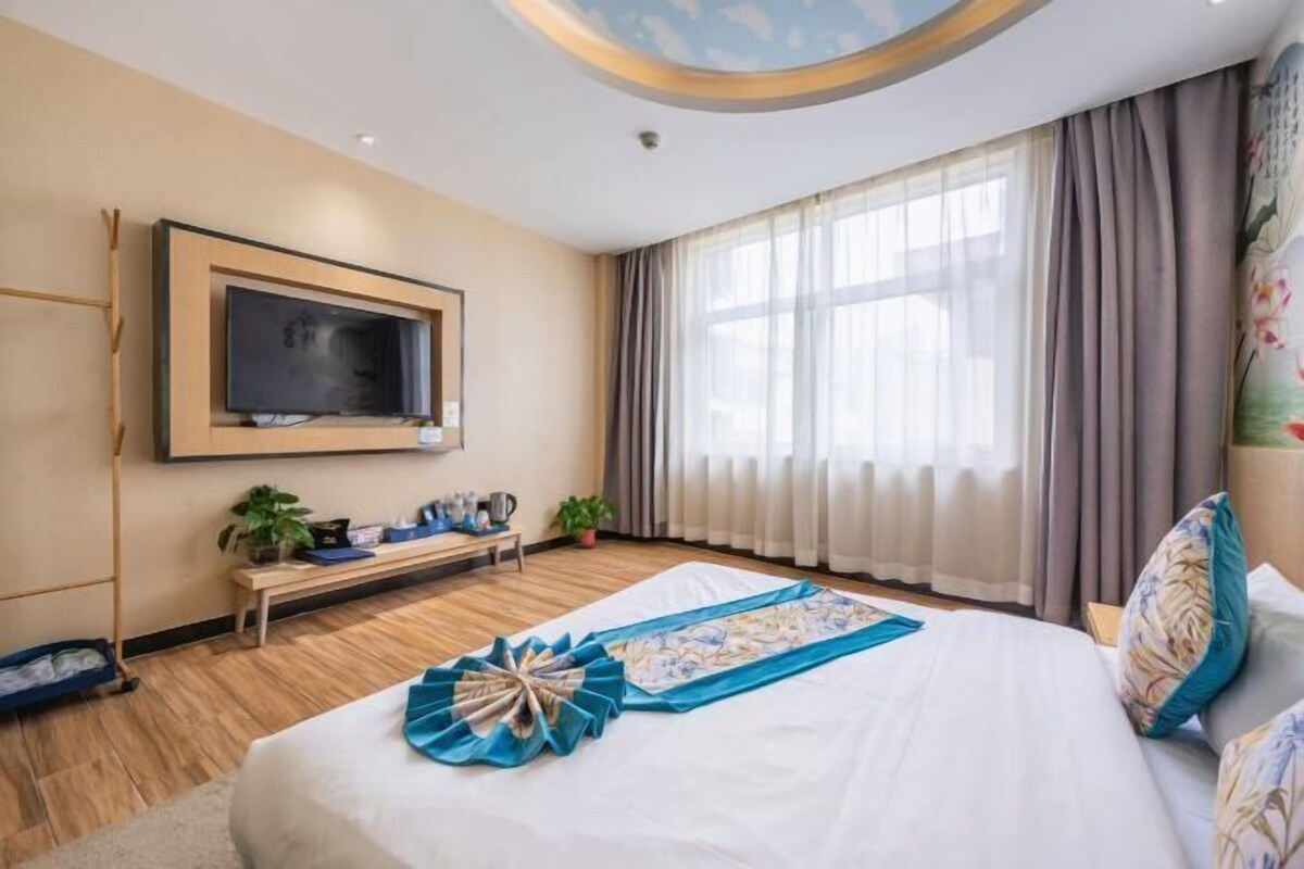 A hotel room with a bed, a television, a desk, and a window with curtains.