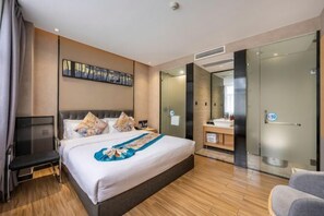 Ein modernes Hotelzimmer mit einem großen Bett, einem Nachttisch, einem Fernseher, einem Badezimmer mit Glastür und einem an der Wand befestigten Kunstwerk.