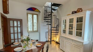 Un comedor con una mesa de madera dispuesta para cuatro personas, un armario blanco con puertas de vidrio y una escalera de caracol.