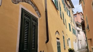 Una calle estrecha con edificios amarillos, contraventanas verdes y un tubo a la vista en la pared.
