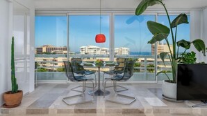 Uma sala de jantar moderna com mesa e cadeiras, grandes janelas com vista para a cidade e um vaso de planta.
