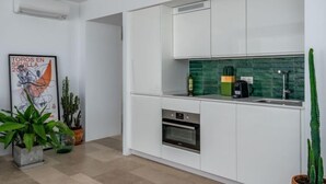 Uma cozinha moderna com armários brancos, painel de parede verde e forno embutido. Há plantas em vasos e um quadro na parede.