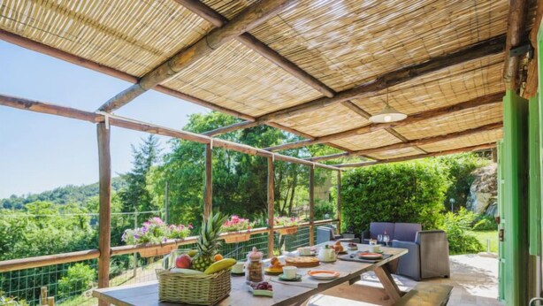 Un área de comedor al aire libre con techo de bambú, bancos de madera y una mesa dispuesta con comida y bebidas.