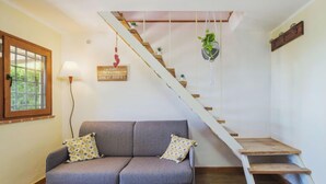 Un salón con sofá gris, escalera de madera y ventana con vista a zonas verdes.