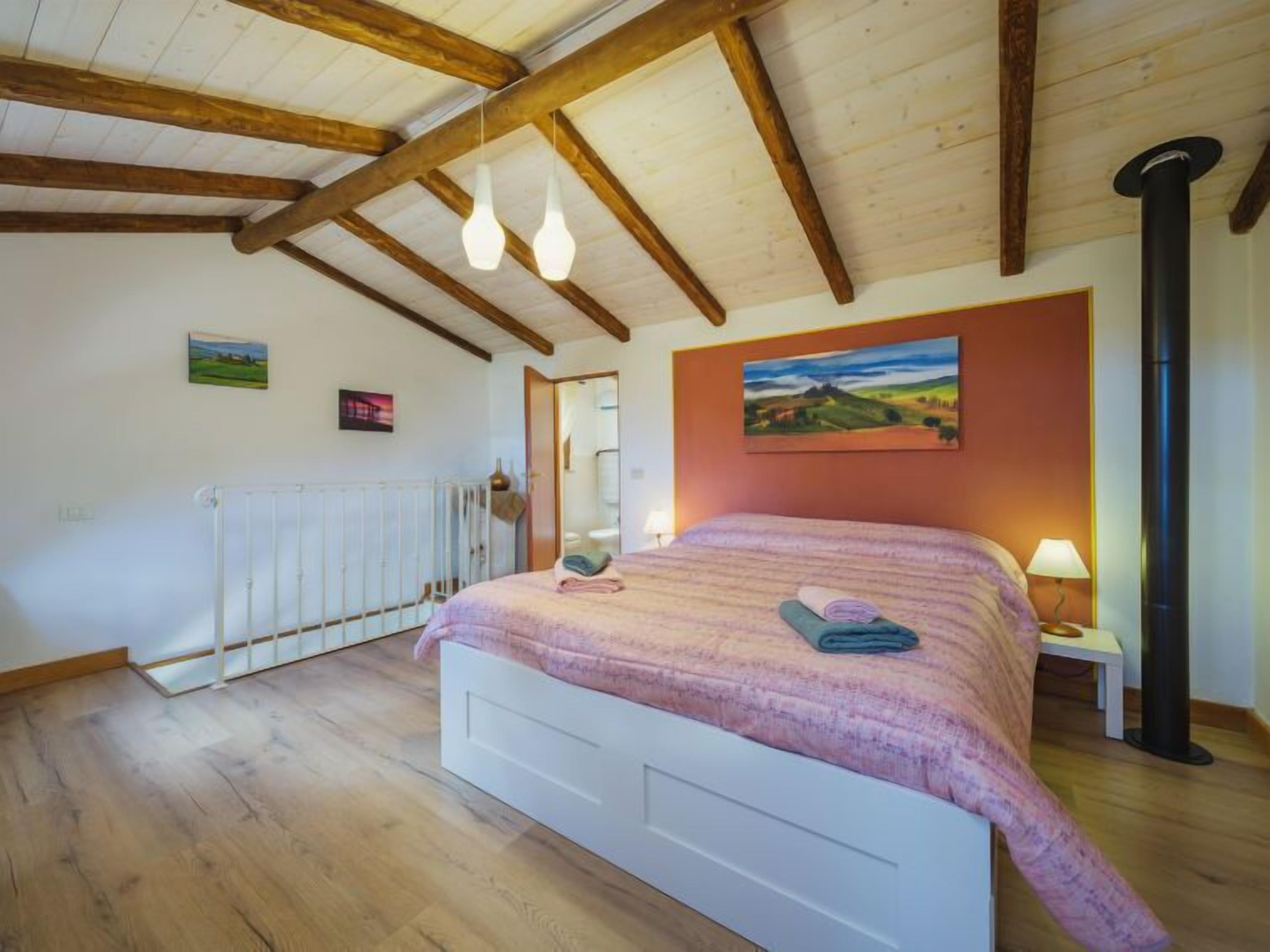 Une chambre avec un plafond en bois, un lit recouvert d’une couverture rose, un radiateur et un tableau accroché au mur.