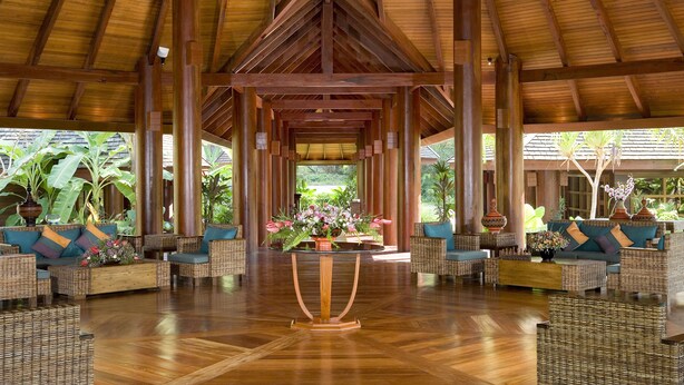 A spacious lobby with a high wooden ceiling, wicker furniture, and a central table with floral arrangements. - One Myanmar Resort Ngapali (Ngapali)