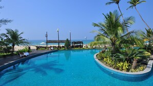 A pool with a clear view of the ocean, surrounded by palm trees and lounge chairs. - One Myanmar Resort Ngapali (Ngapali)