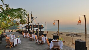 A beachside dining area with tables and chairs, umbrellas, and a wooden deck overlooking the ocean. - One Myanmar Resort Ngapali (Ngapali)