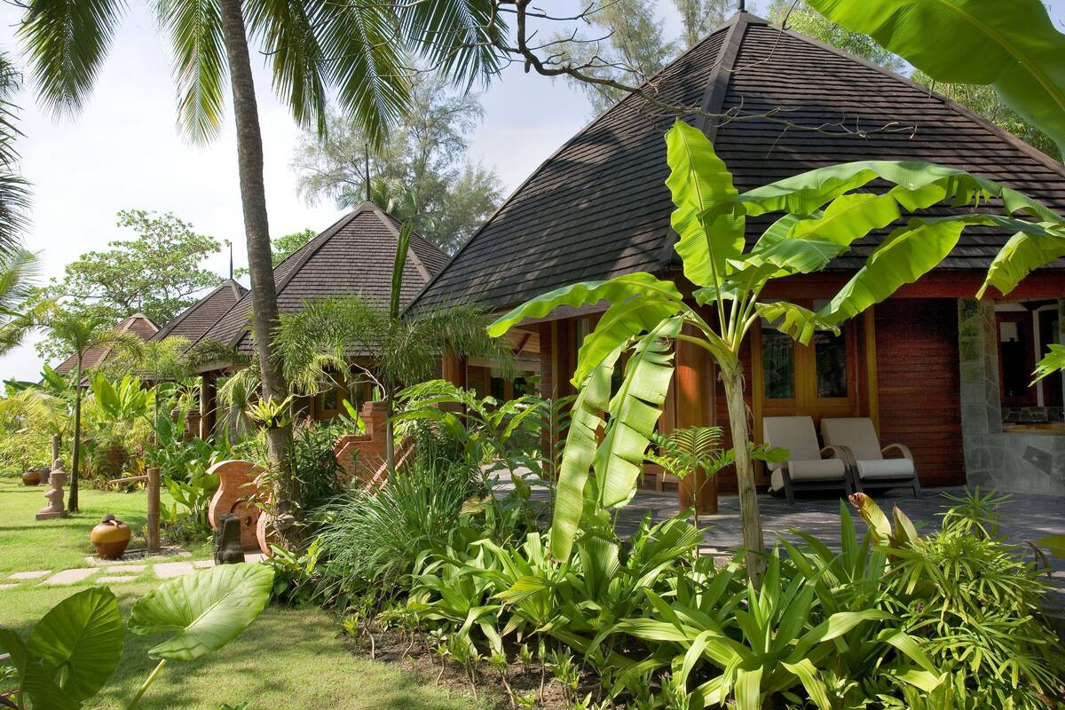 A resort with multiple bungalow-style buildings, lush tropical gardens, and a well-maintained lawn.