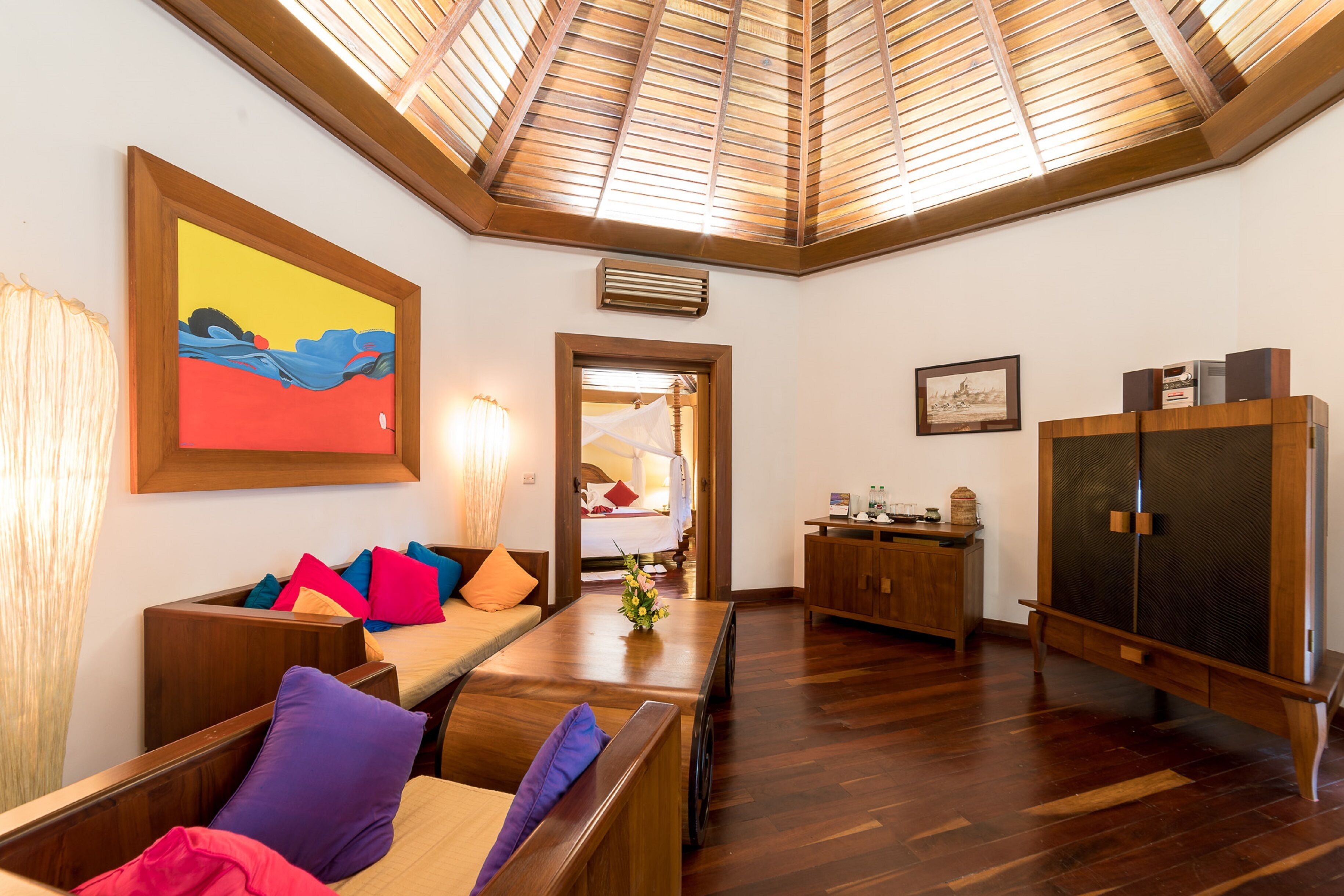 Una habitación con techo de madera, una cama, un banco de madera, una pequeña mesa con un jarrón y un armario.