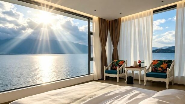 A hotel room with a large bed, two chairs, a small table, and a view of a body of water. - Hersy Vista · Hesi 270° Panoramic Erhai-Cangshan View Boutique Stay (Dali City)