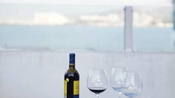 A bottle of wine and two glasses on a table with a view of a body of water and buildings in the background.