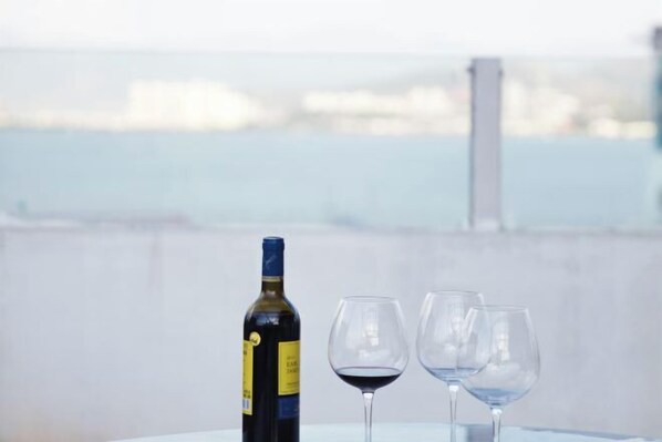 A bottle of wine and two glasses on a table with a view of a body of water and buildings in the background. - Hersy Vista · Hesi 270° Panoramic Erhai-Cangshan View Boutique Stay (Dali City)