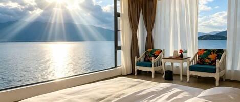 A hotel room with a large bed, two chairs, a small table, and a view of the sea.