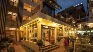 A modern hotel with a glass facade, outdoor seating area, and a well-maintained garden. - Hersy Vista · Hesi 270° Panoramic Erhai-Cangshan View Boutique Stay (Dali City)