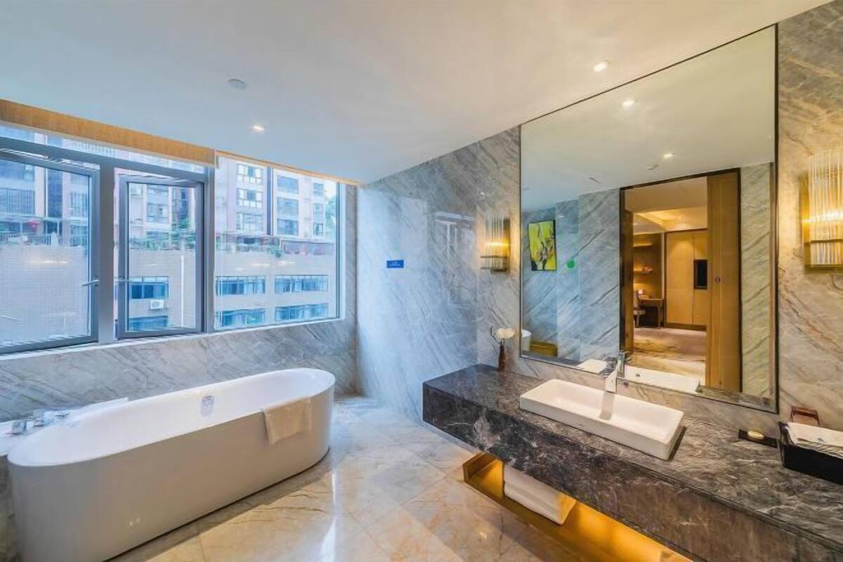 Ein modernes Badezimmer mit Badewanne, Waschtisch mit Spiegel und Blick ins Freie.